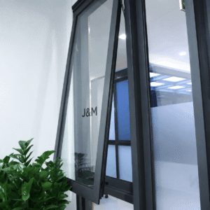 Close-up of a modern black aluminium awning window, partially open, with glass panels and green plants beside the window.